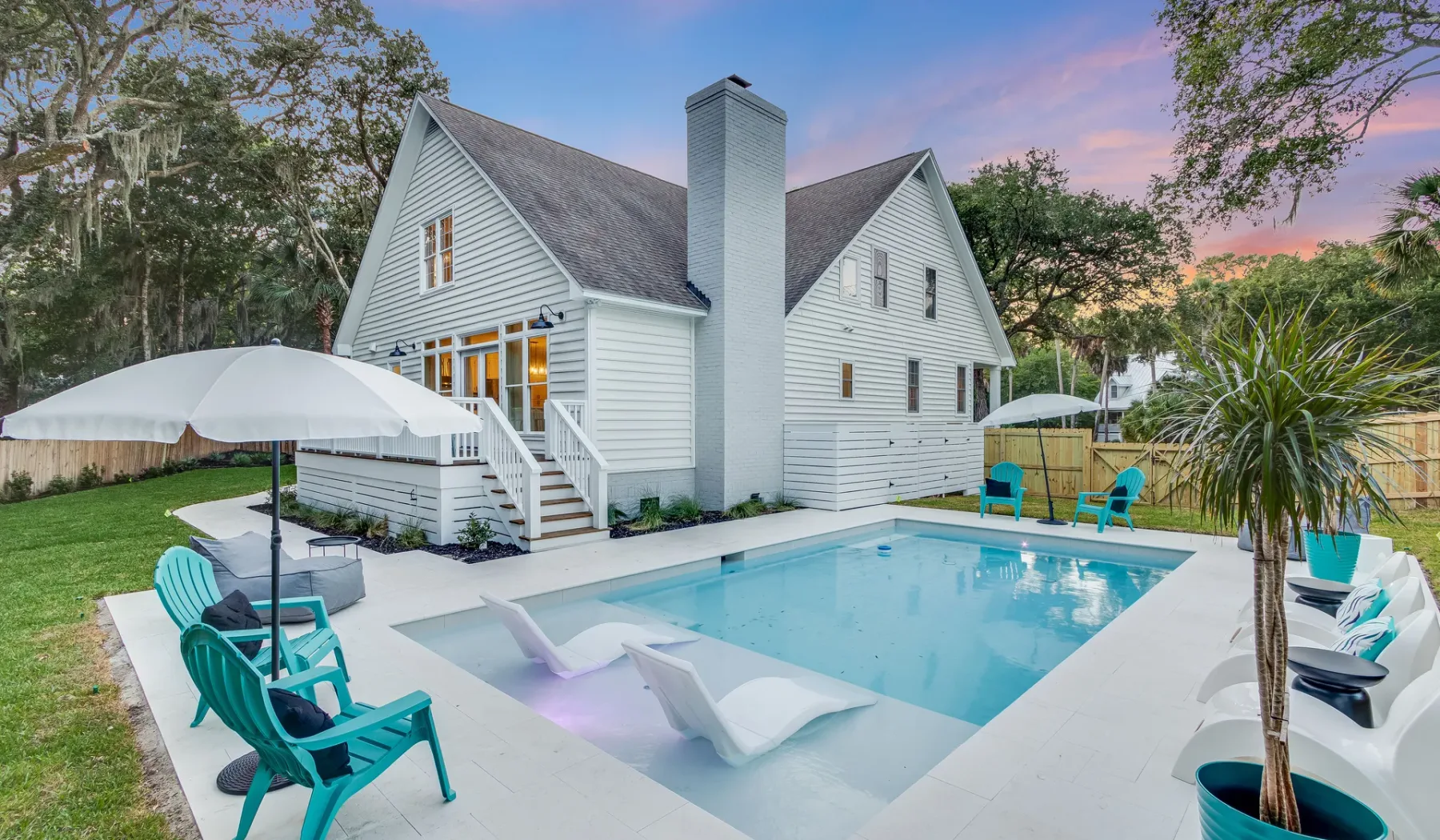 Una casa blanca da a una piscina con asientos reclinables y sombrillas.