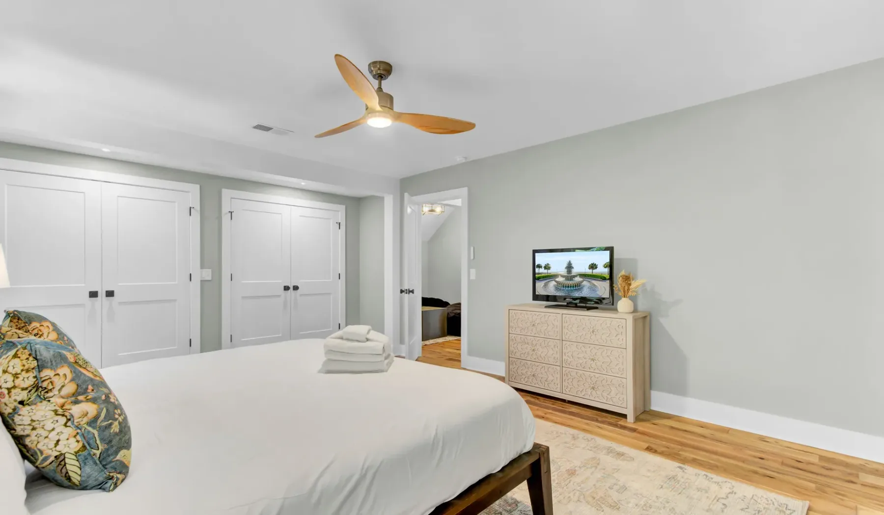 A bright bedroom with a neatly made bed and a dresser beneath a television.