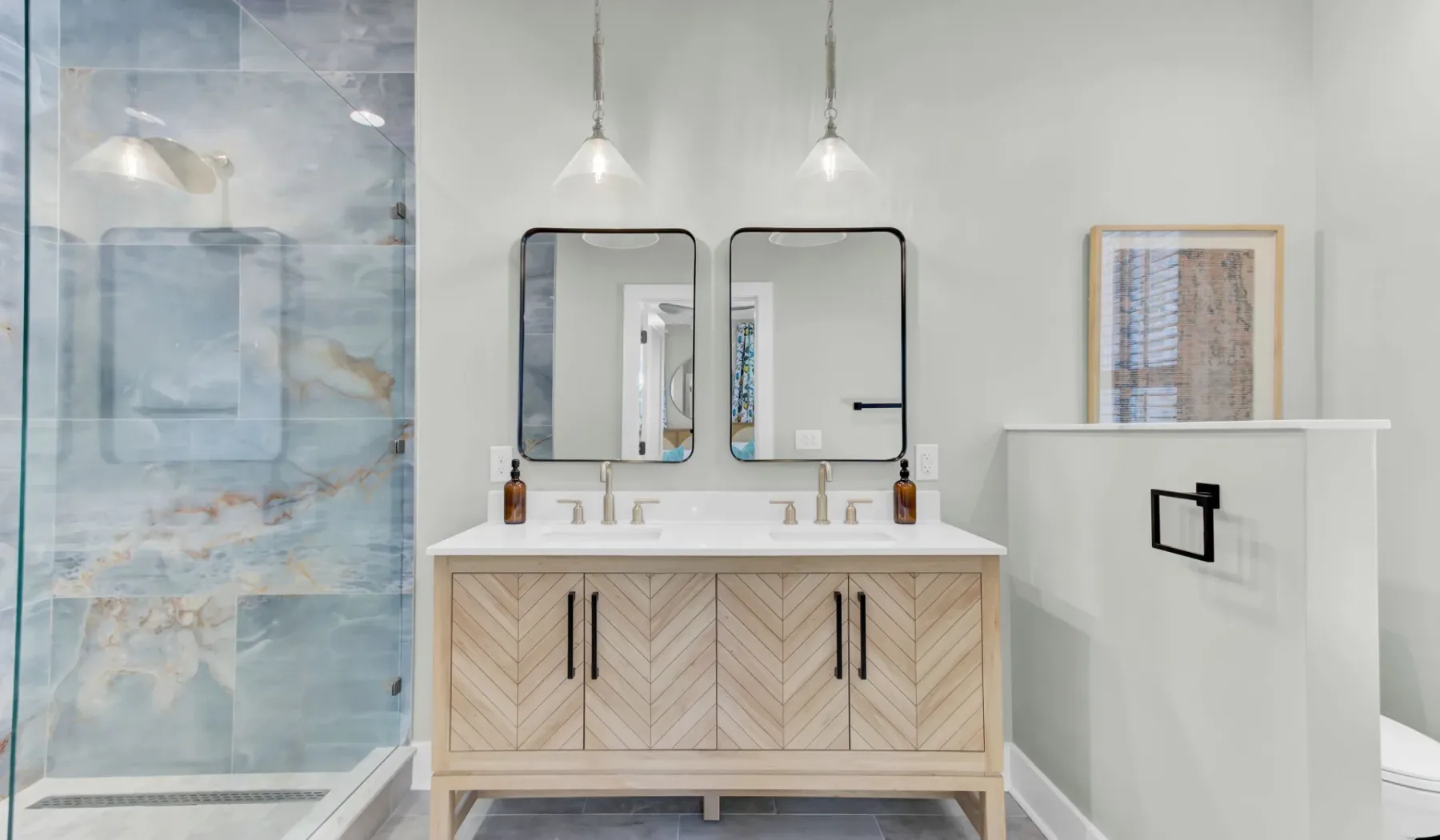 A bright bathroom with a glass shower, double sink vanity, and framed wall art.