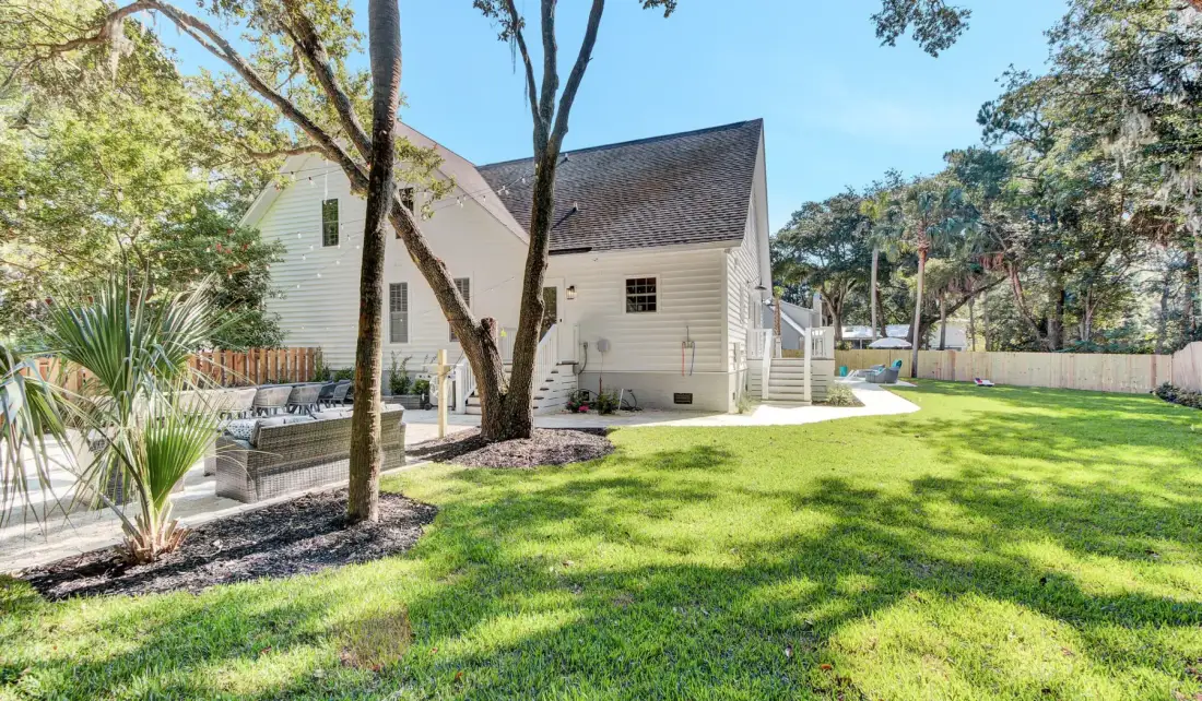 A white house faces a sunny lawn, with trees and a paved patio.
