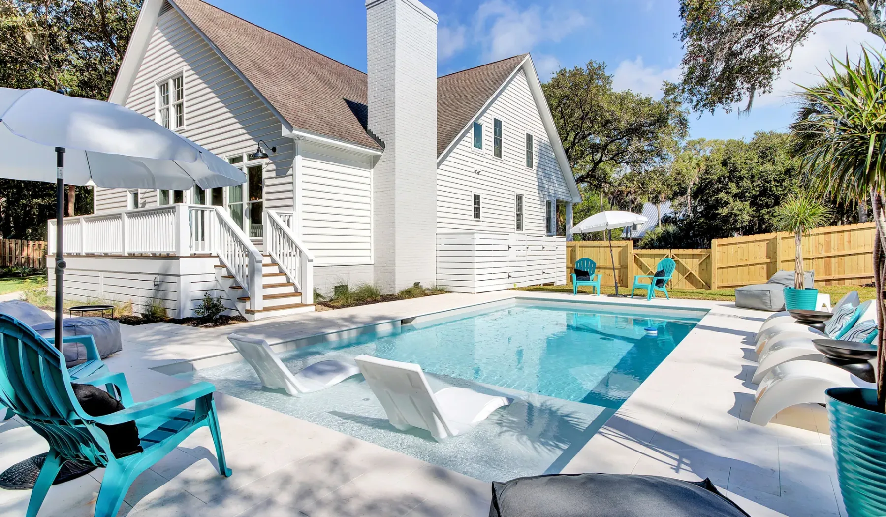 A swimming pool sits beside a white house, with turquoise seating around the patio.