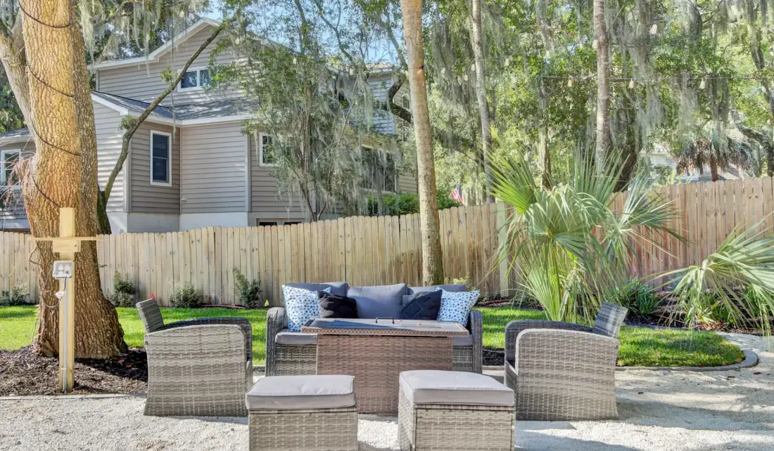 An outdoor patio seating area with wicker furniture beside a fenced yard.