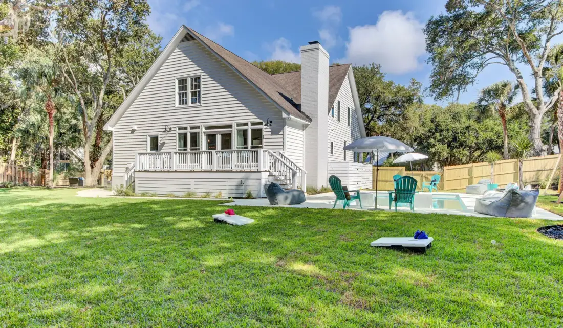 A large house stands beside a swimming pool, with a grassy lawn in front.