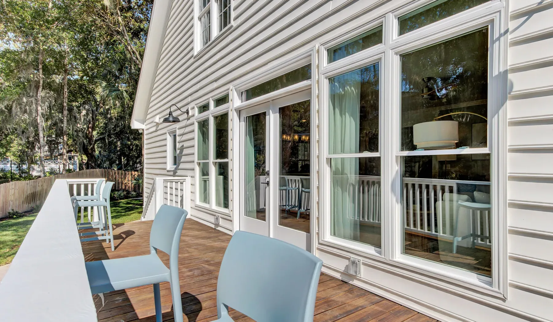 A wooden deck with outdoor seating runs alongside a house with large windows.