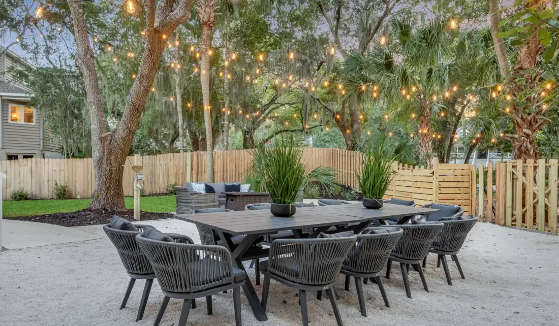 An outdoor dining area with a long table and string lights among the trees.