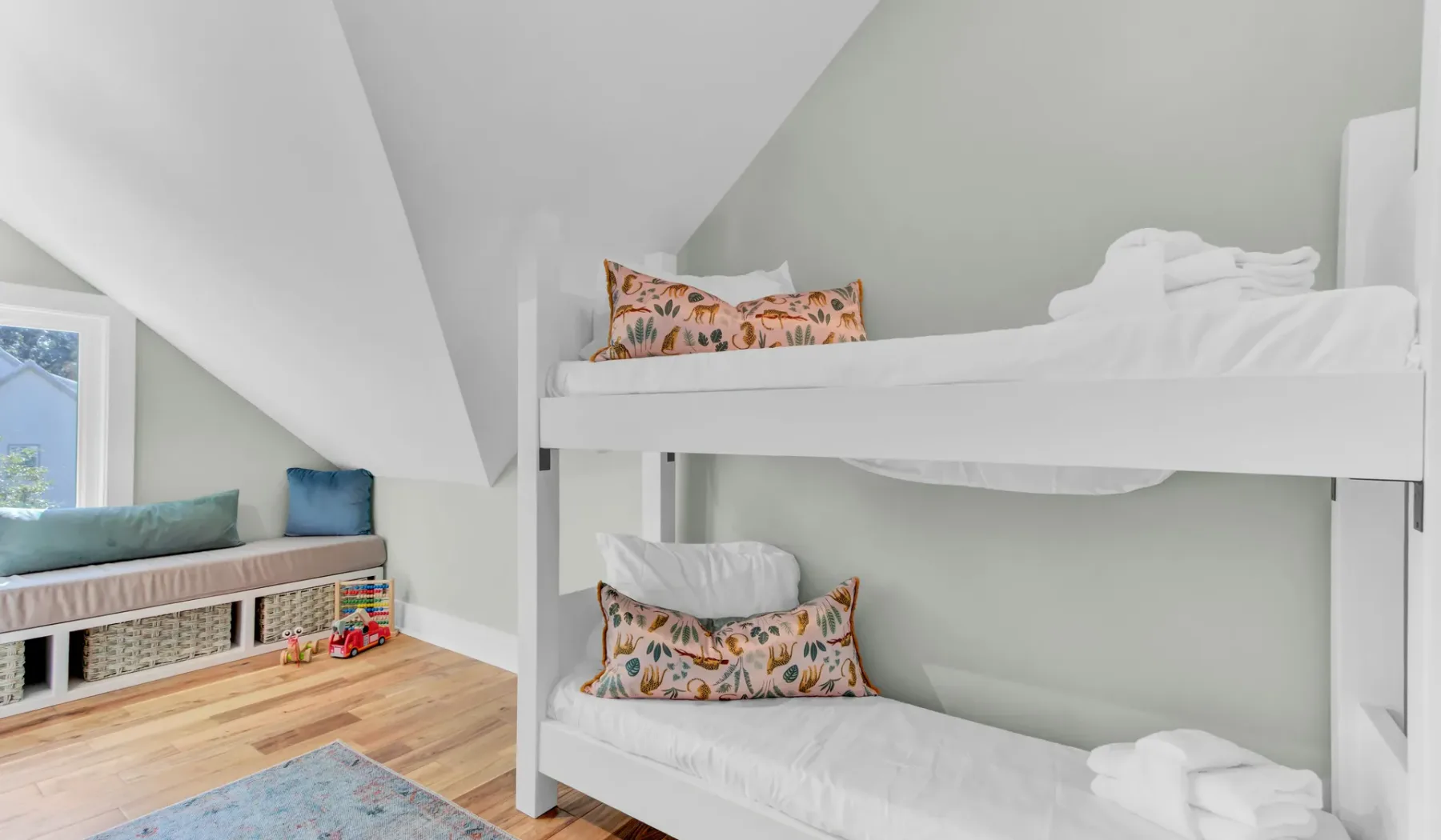 A bunk bed with patterned pillows sits beside a window seat in a bright bedroom.