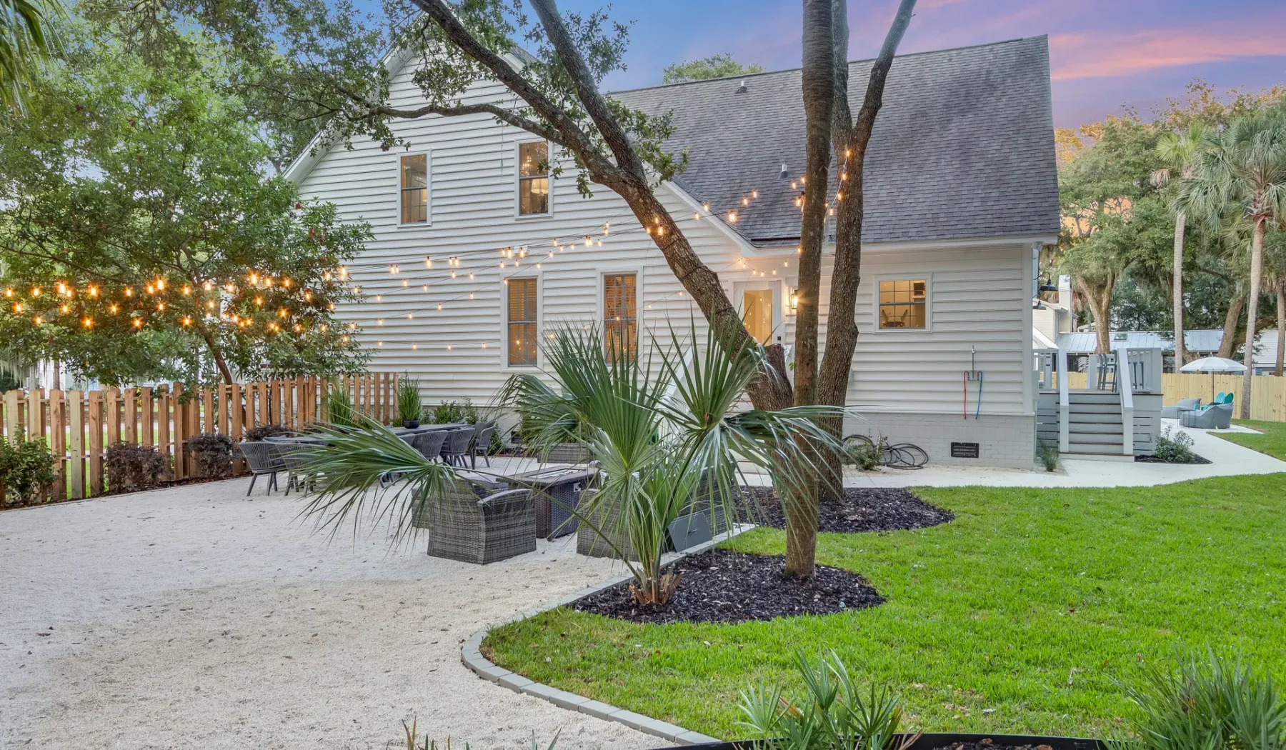 A white house stands beside an outdoor seating area and landscaped lawn.