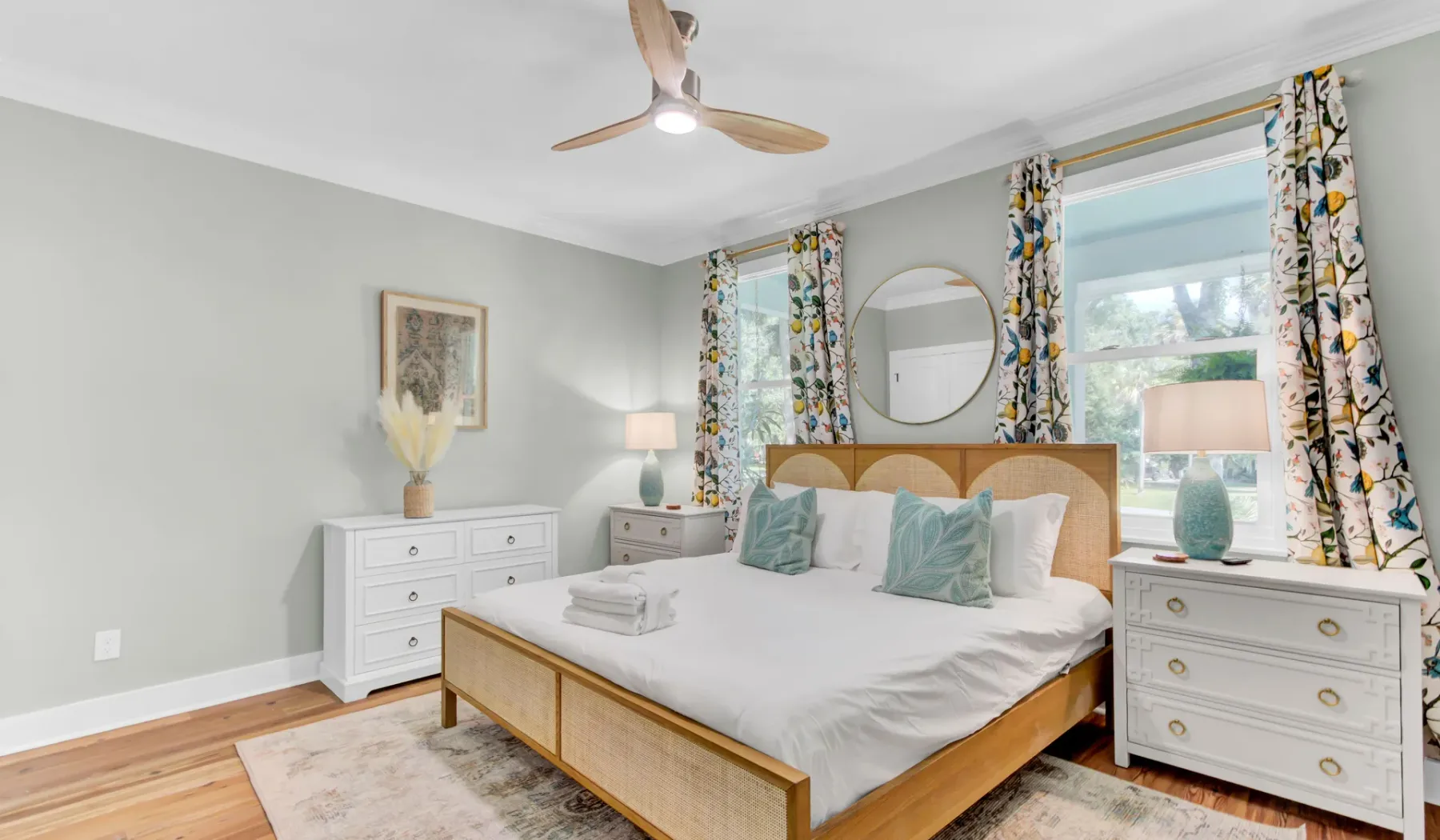 A bedroom with a bed, matching dressers, and floral curtains.