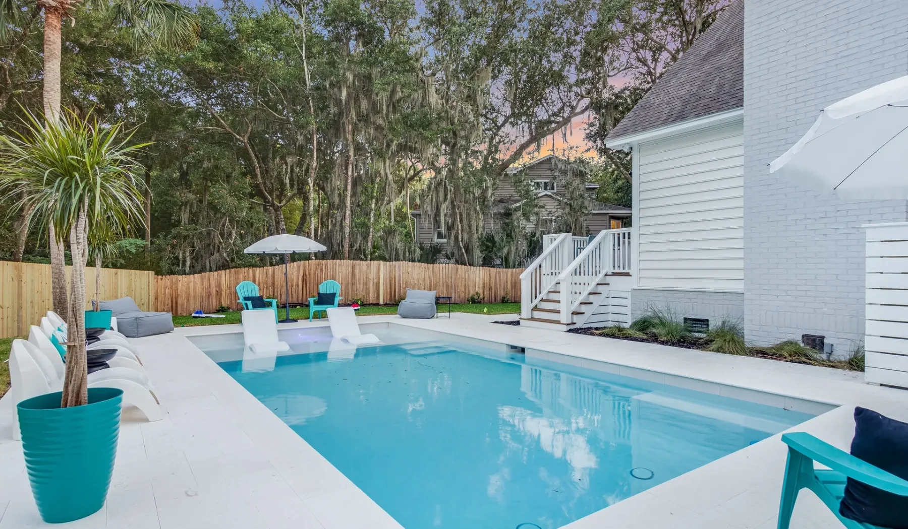An outdoor swimming pool beside a white house, with lounge seating around the deck.