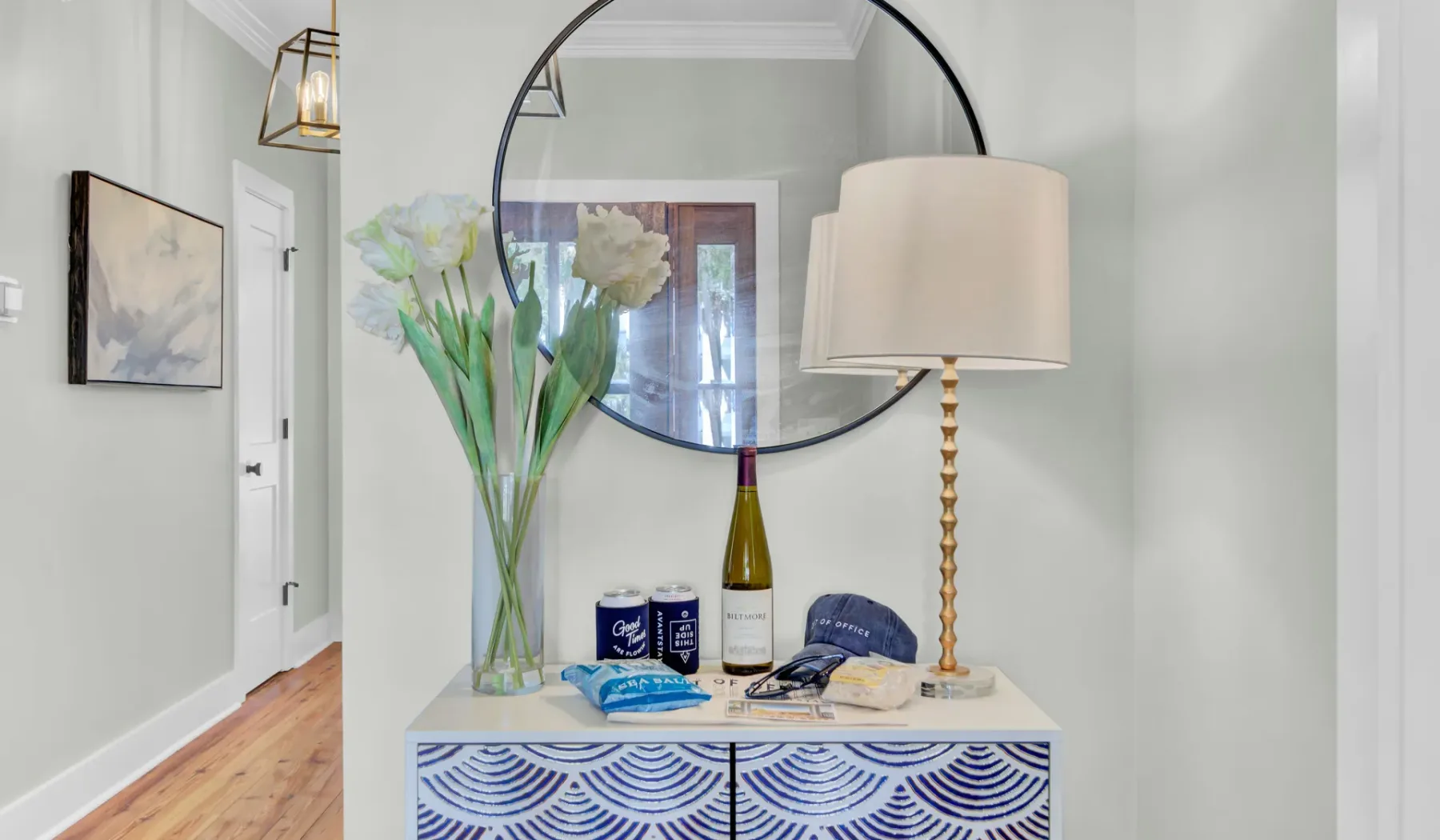 A console table with flowers and a lamp sits beneath a large round mirror.