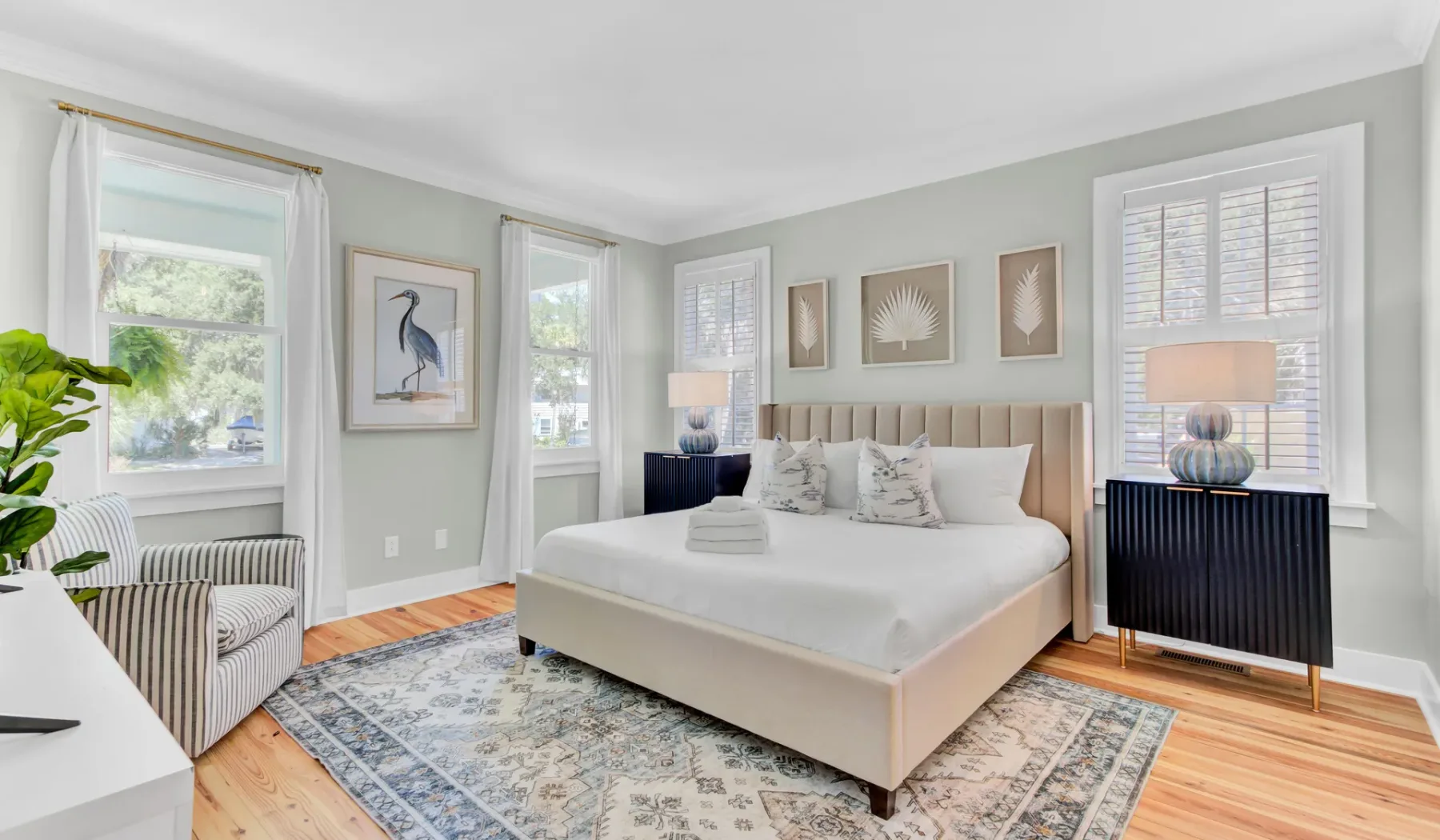 A bright bedroom with a neatly made bed, pale walls, and large windows.
