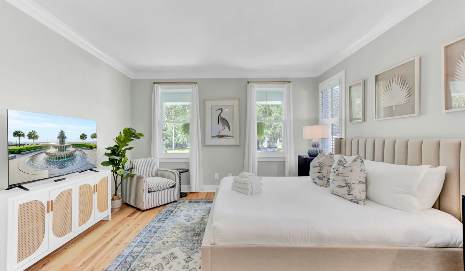 A bright bedroom features a large bed, a sitting area, and framed artwork.