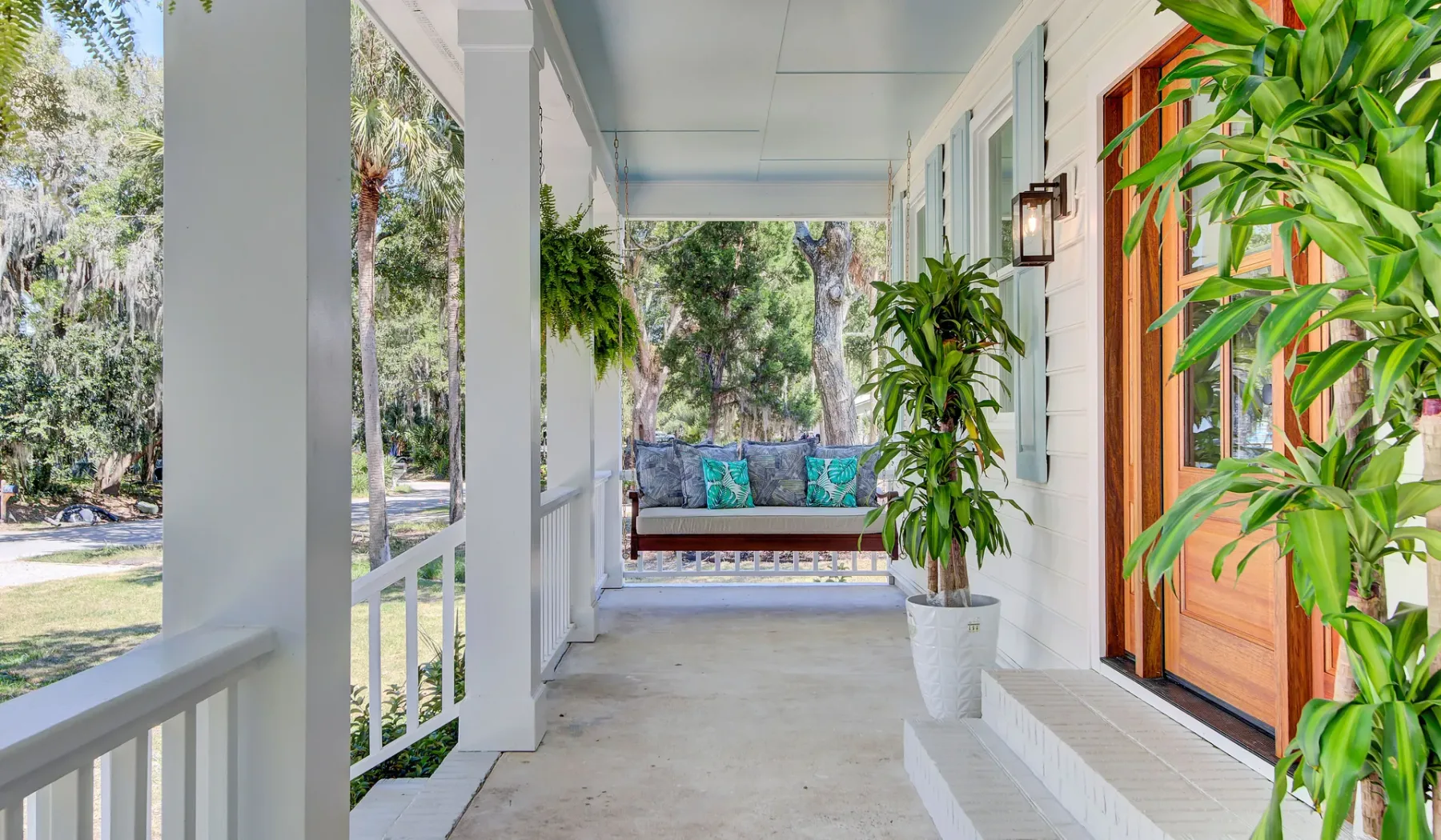 A covered porch with seating and potted plants overlooks a leafy yard.
