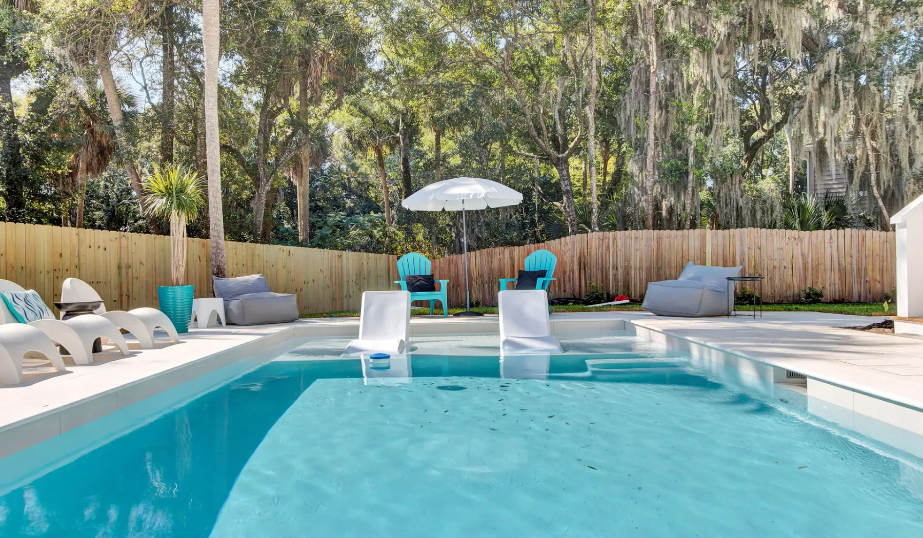 An outdoor swimming pool with lounge seating and an umbrella on the deck.