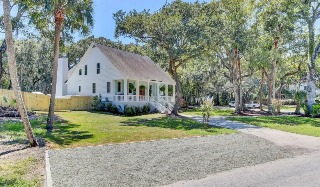 A white house sits among trees beside a paved driveway and green lawn.