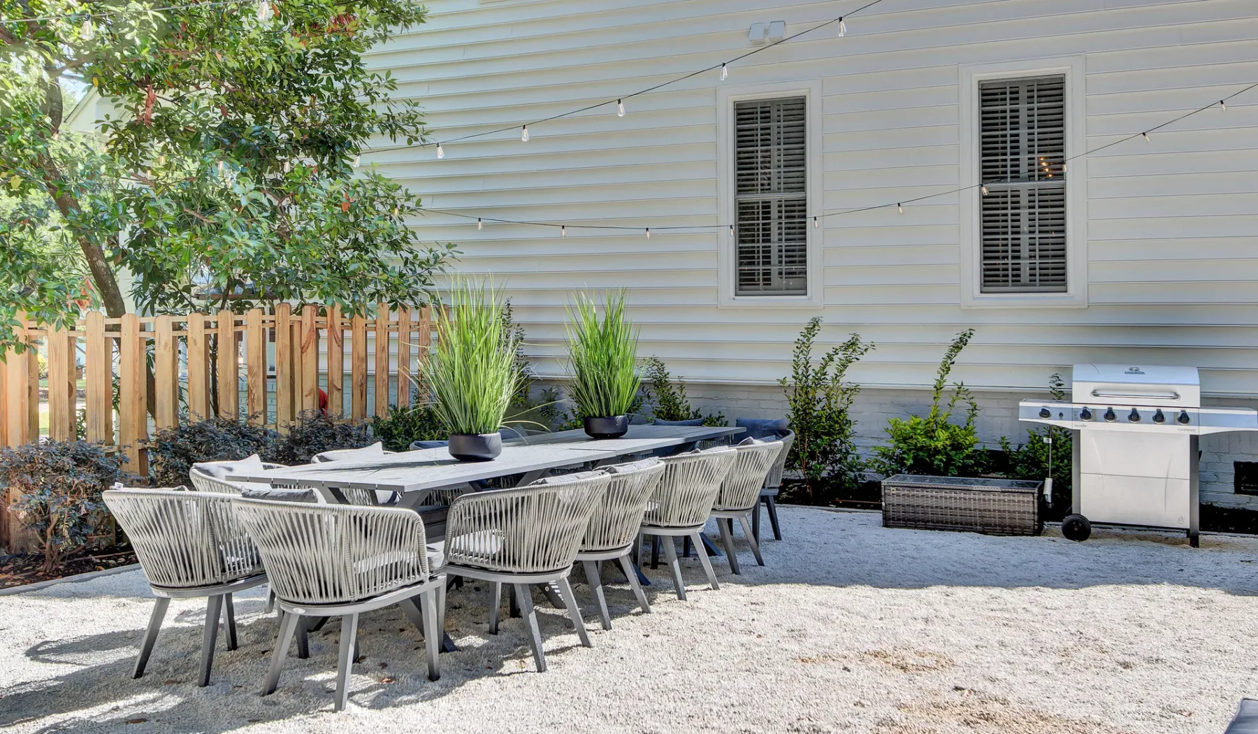 An outdoor dining area with a long table, seating, and a grill.