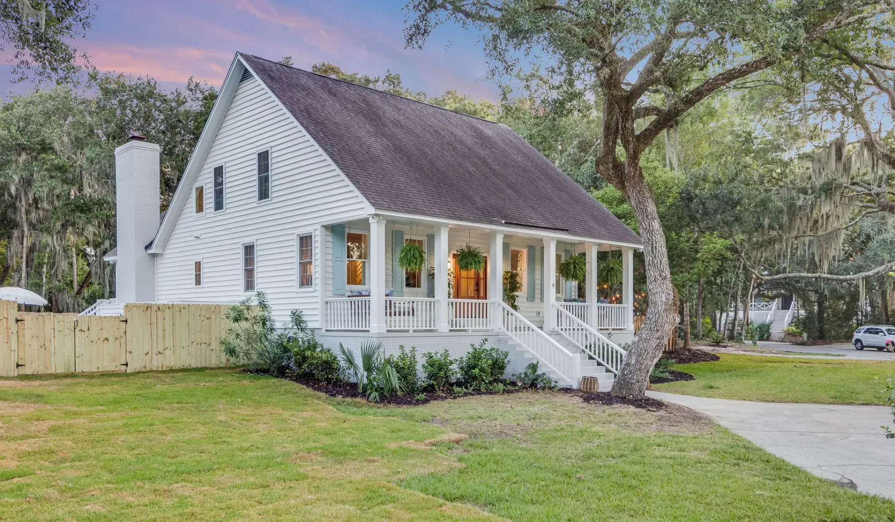 A white house with a covered front porch sits beside a grassy yard.