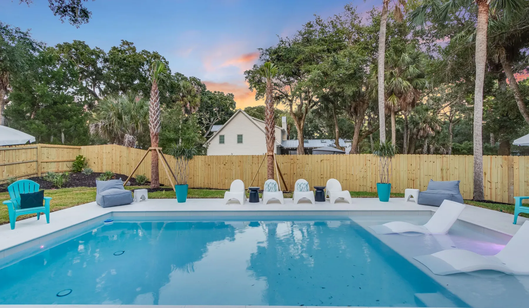 An outdoor swimming pool with lounge seating beside a wooden fence.