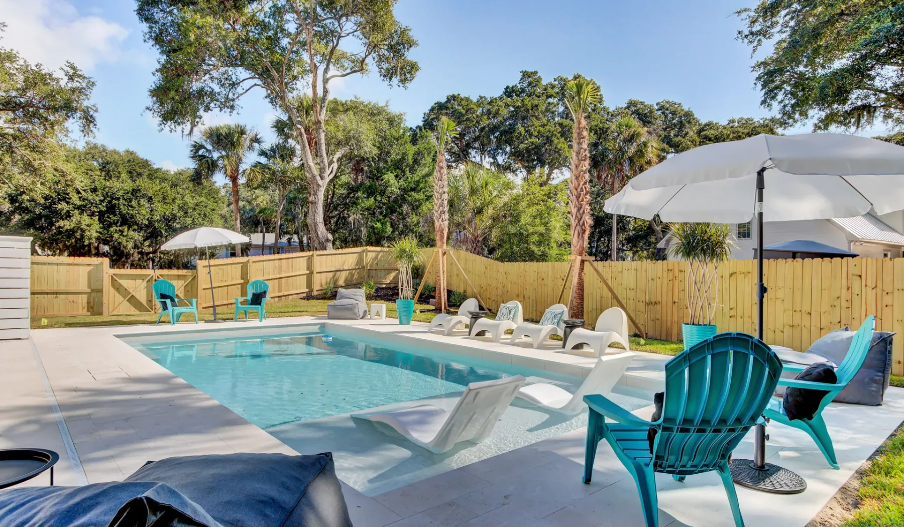 An outdoor swimming pool is surrounded by lounge seating, umbrellas, and trees.