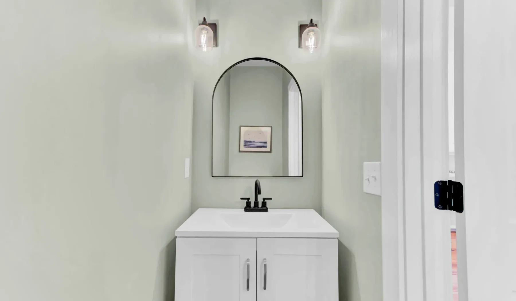 A bathroom vanity with a sink sits beneath an arched mirror.