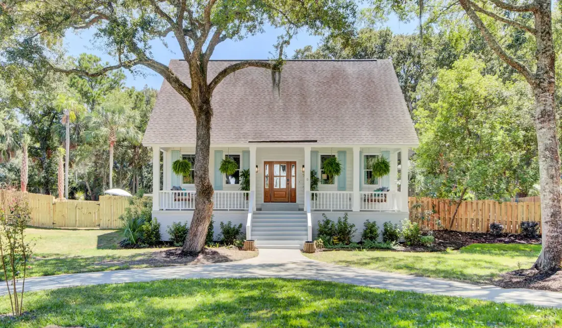 A small house with a front porch stands among trees beside a curved walkway.