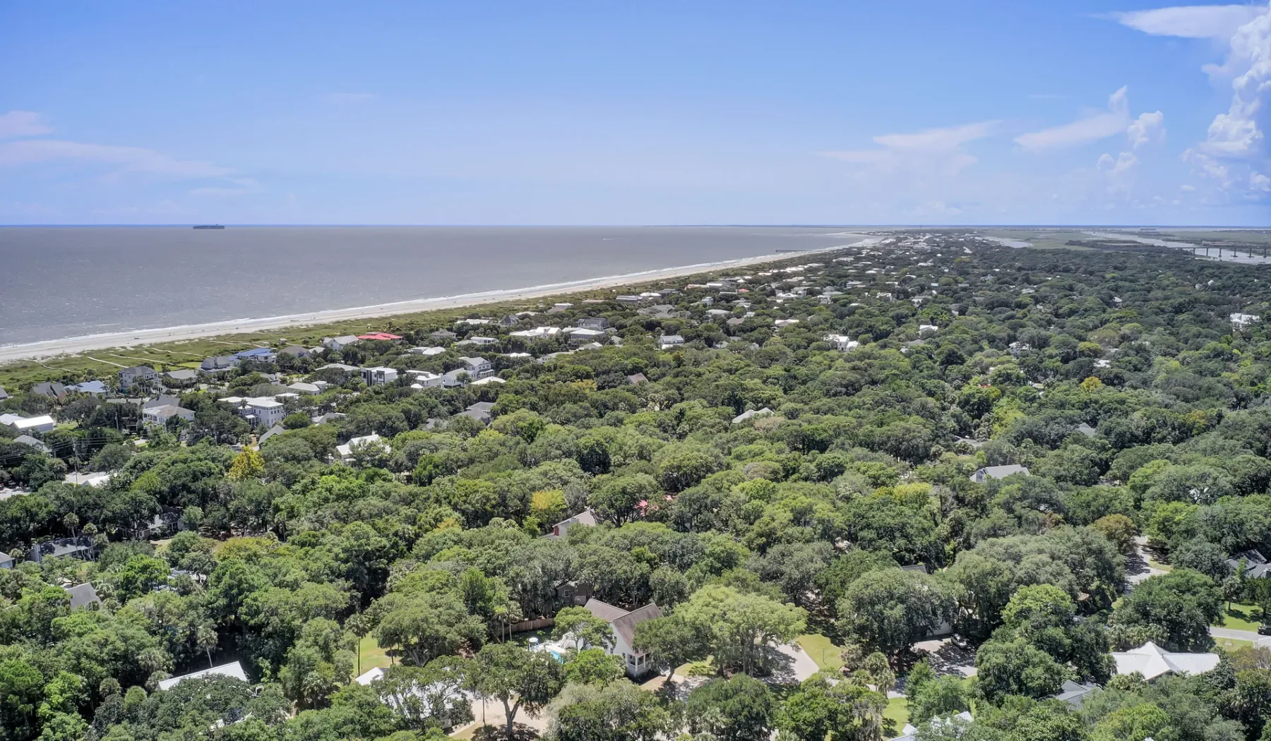An aerial view of a coastal neighborhood bordered by dense greenery and the shoreline.