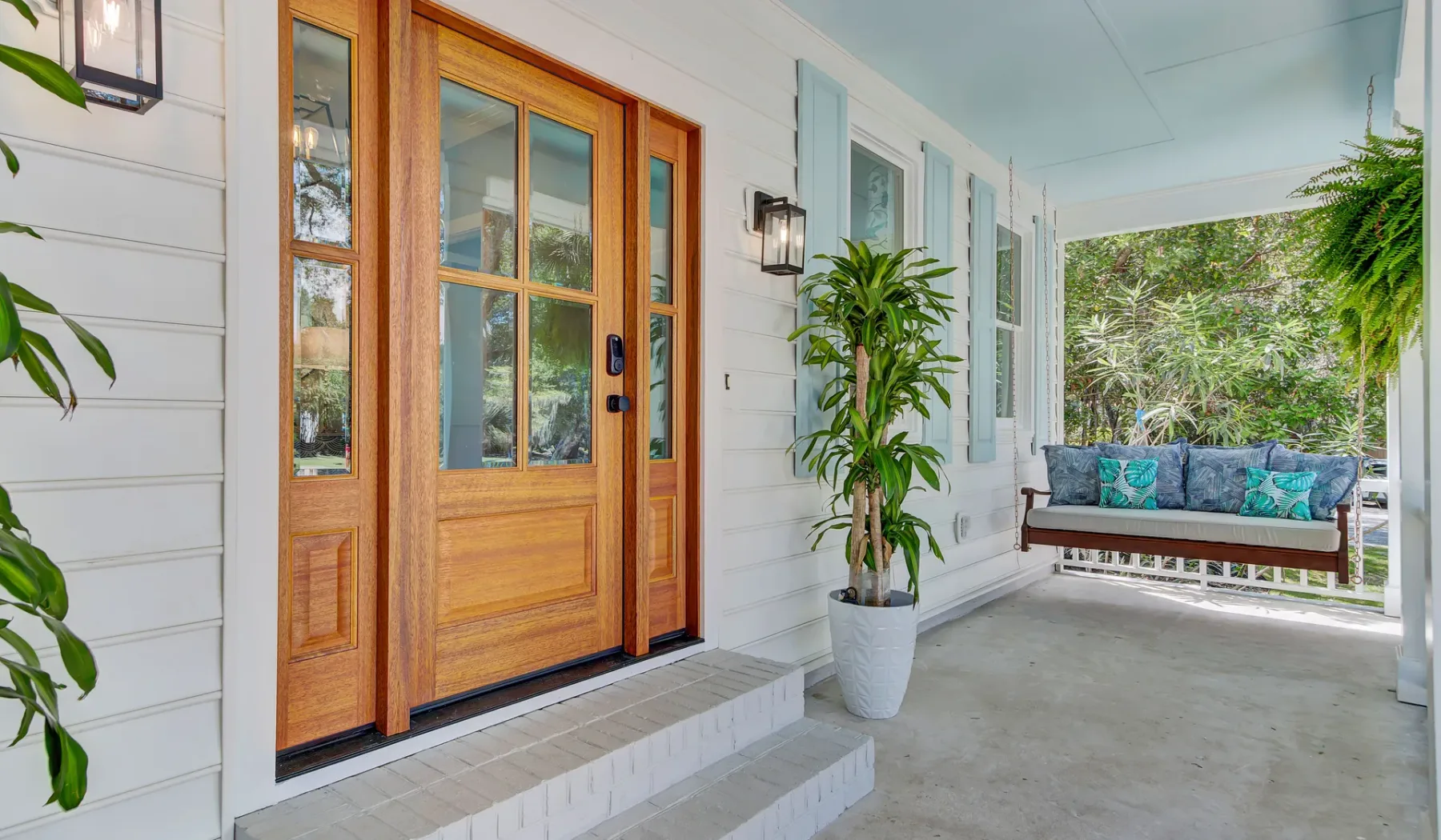 A covered porch with a wooden entry door, potted plants, and outdoor seating.