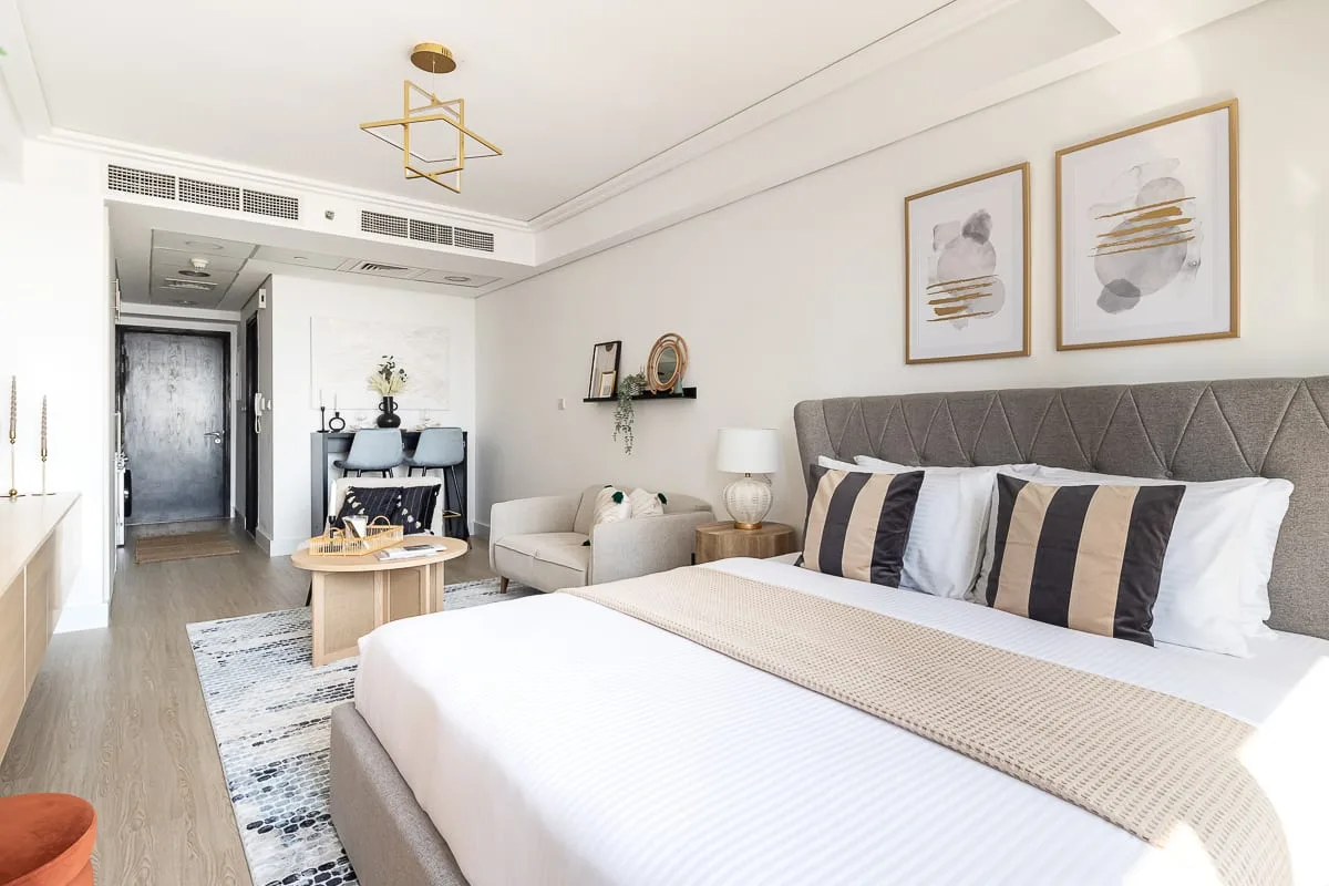 Un dormitorio luminoso con una cama grande, una zona de estar y un escritorio al fondo.