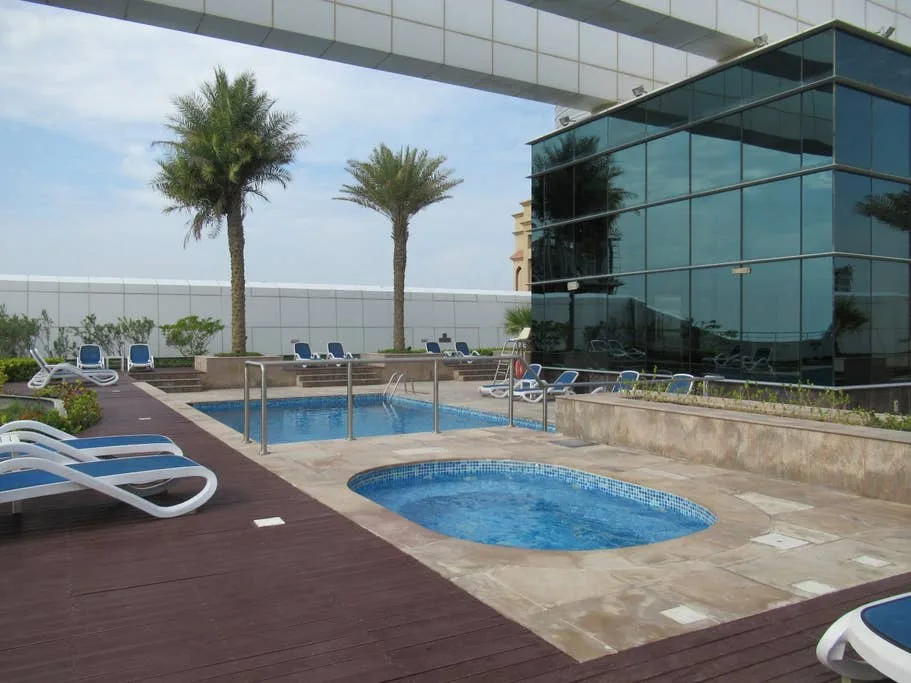 Zona de piscina al aire libre con una piscina redonda más pequeña junto a un edificio con fachada de vidrio.