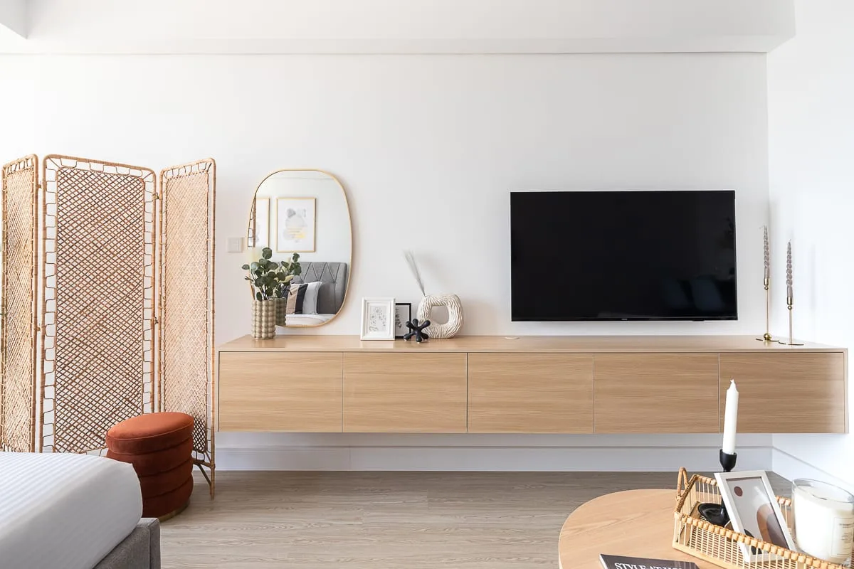 Un dormitorio luminoso con un televisor montado en la pared sobre una consola larga de madera.