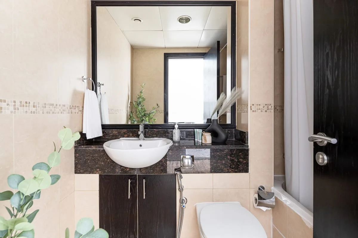 Un baño con lavabo, mueble oscuro y un espejo grande.