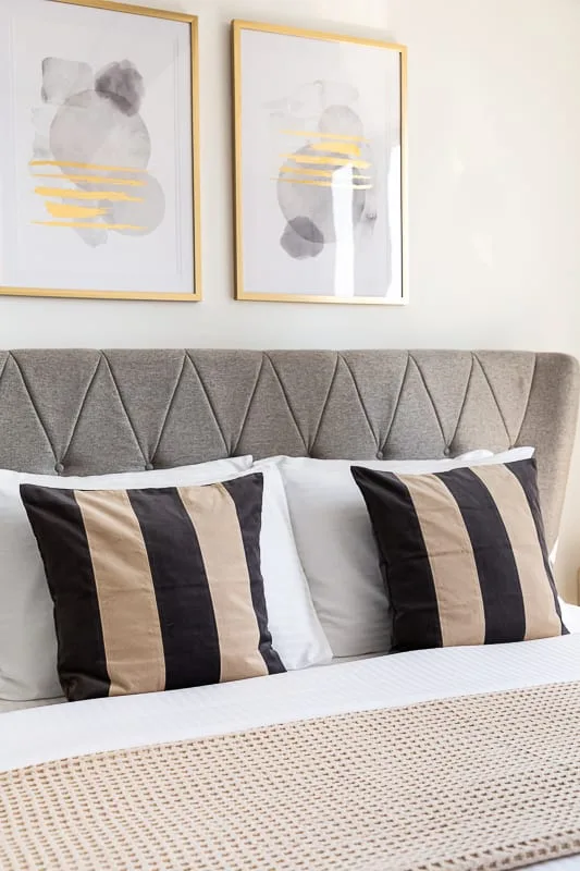 Una cama con almohadas a rayas y arte abstracto sobre el cabecero tapizado.