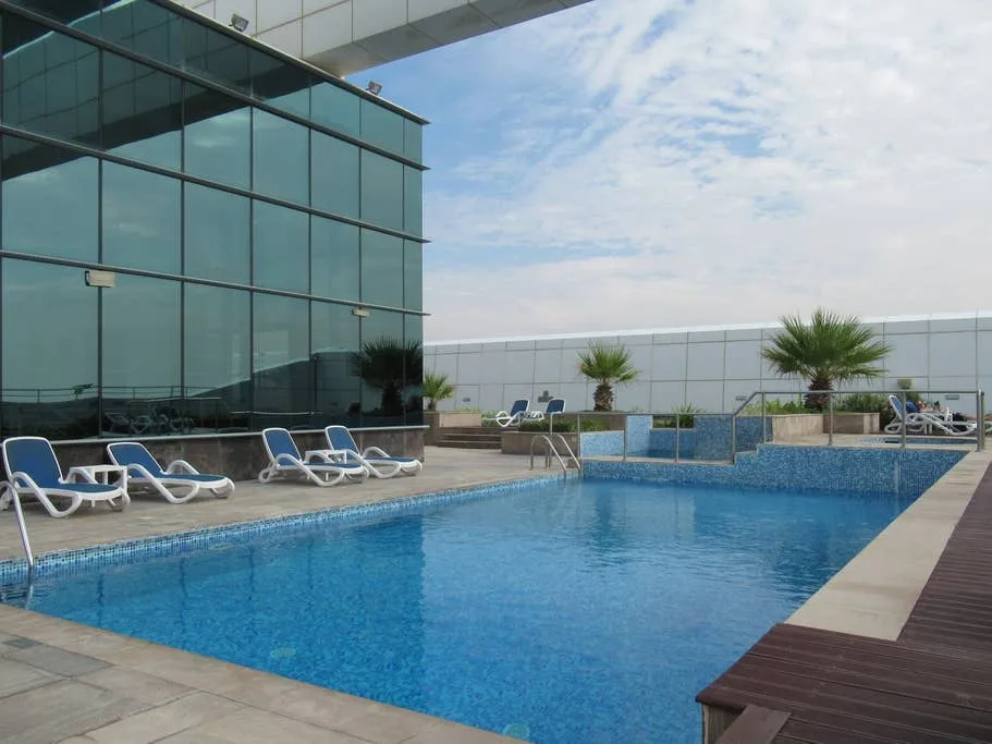 Una piscina al aire libre junto a un edificio acristalado y asientos en la terraza.