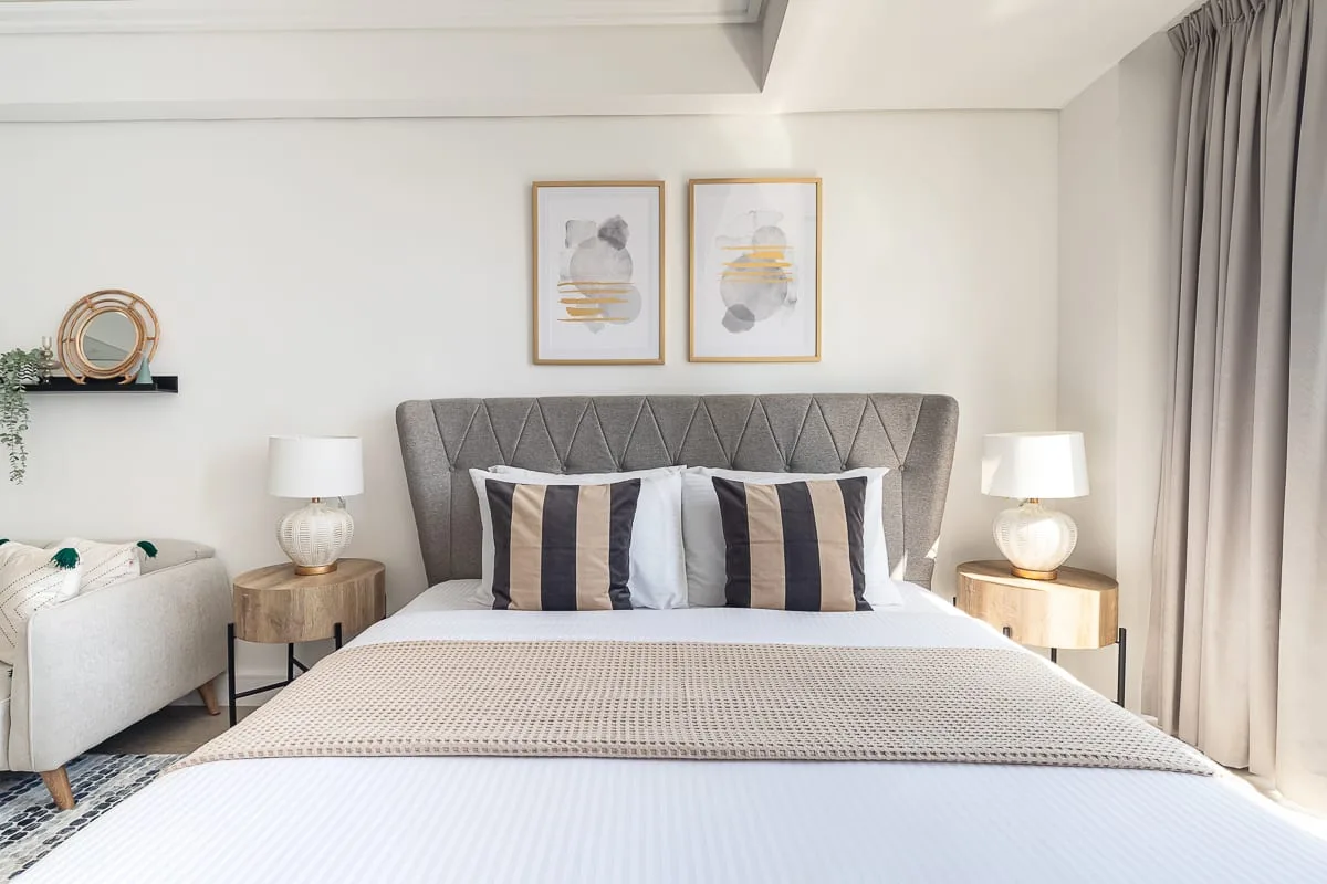 Un dormitorio luminoso presenta una cama bien tendida y cuadros sobre el cabecero.