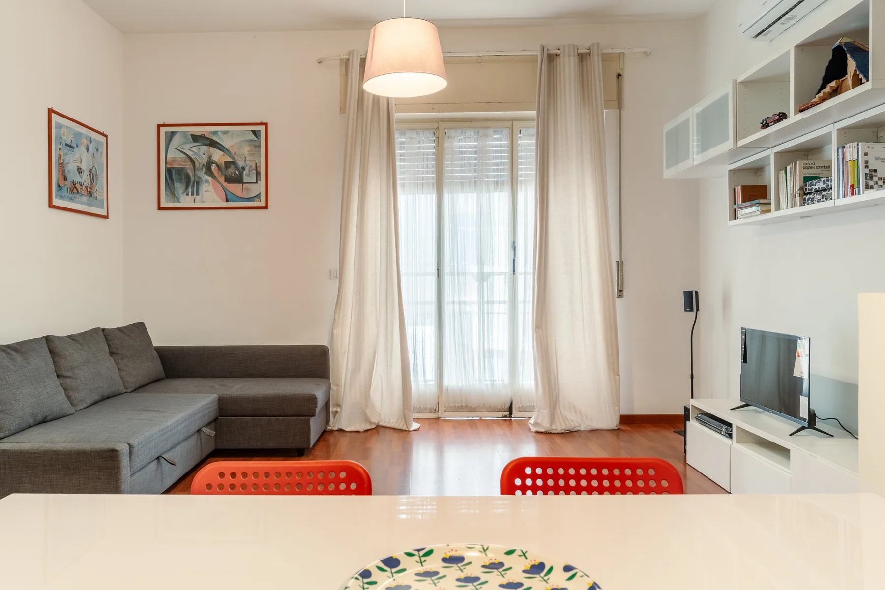 A bright living room with seating, a television, and a glass door framed by curtains.