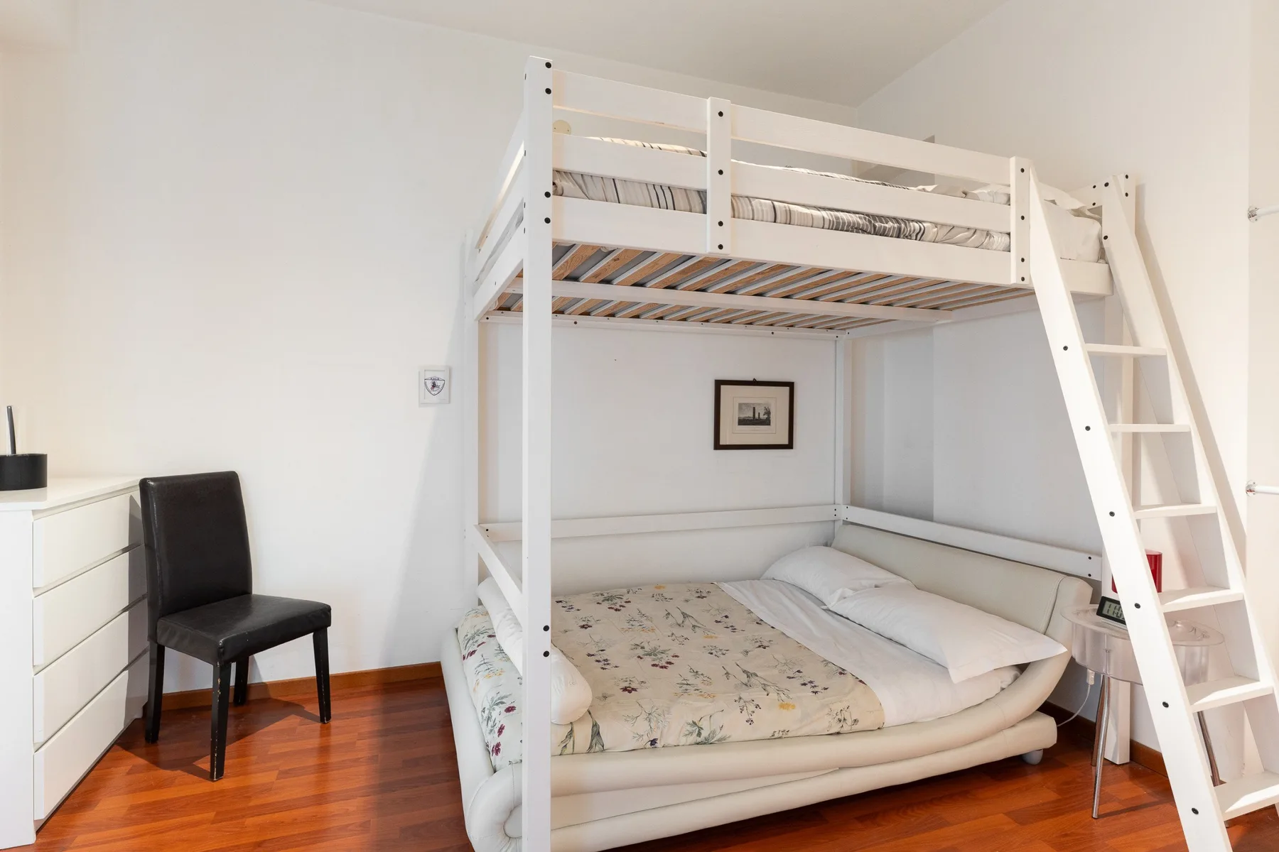 Un dormitorio con una litera blanca, una silla de escritorio y un cuadro enmarcado.