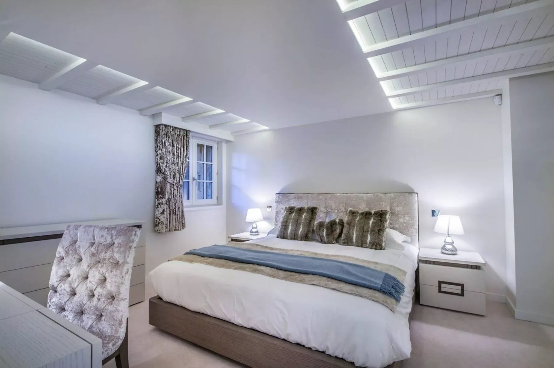 Un dormitorio con una cama, mesitas de noche y una pequeña ventana con cortina.