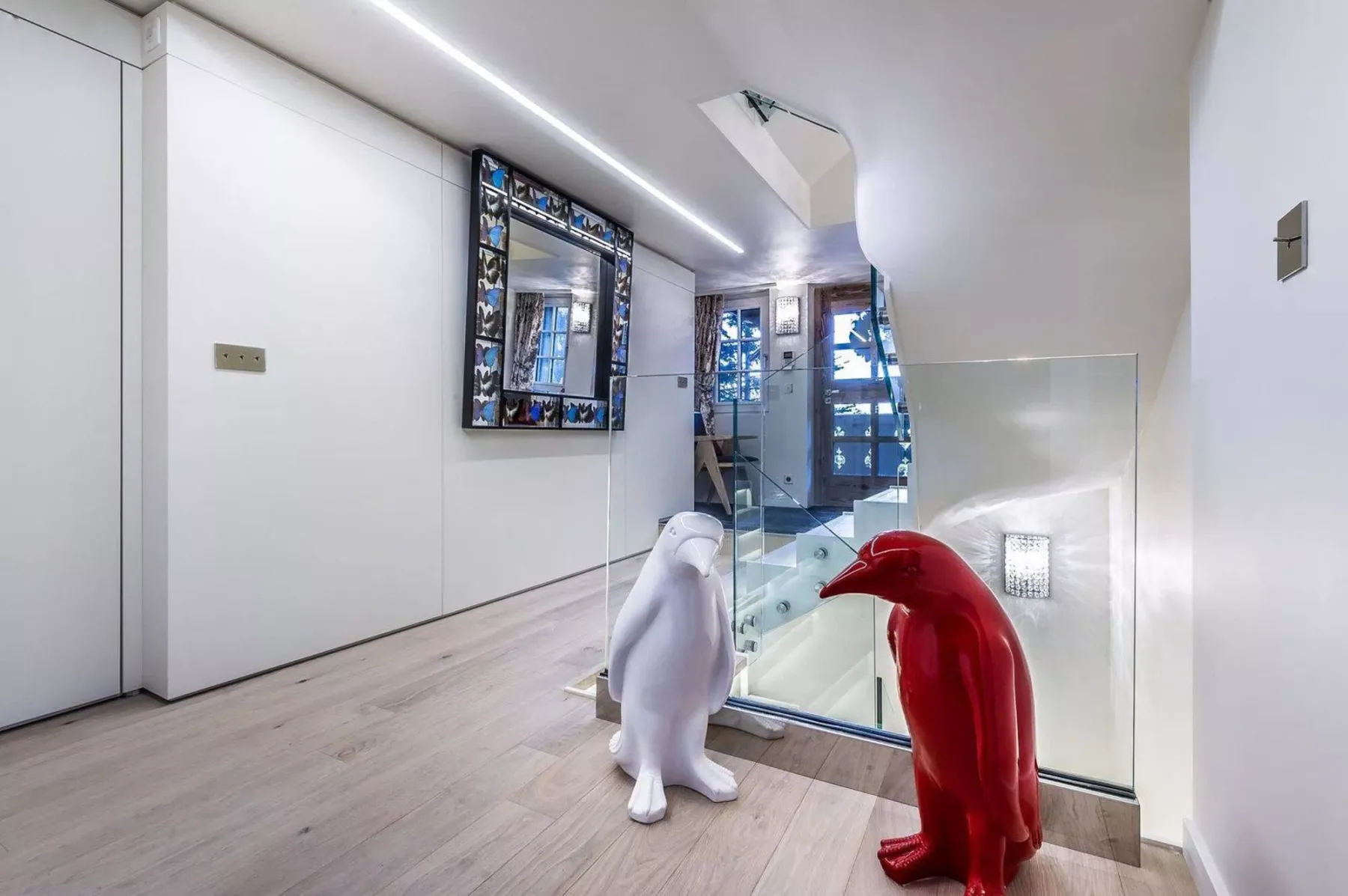 Un pasillo moderno y luminoso con una barandilla de vidrio y dos esculturas de pingüinos.