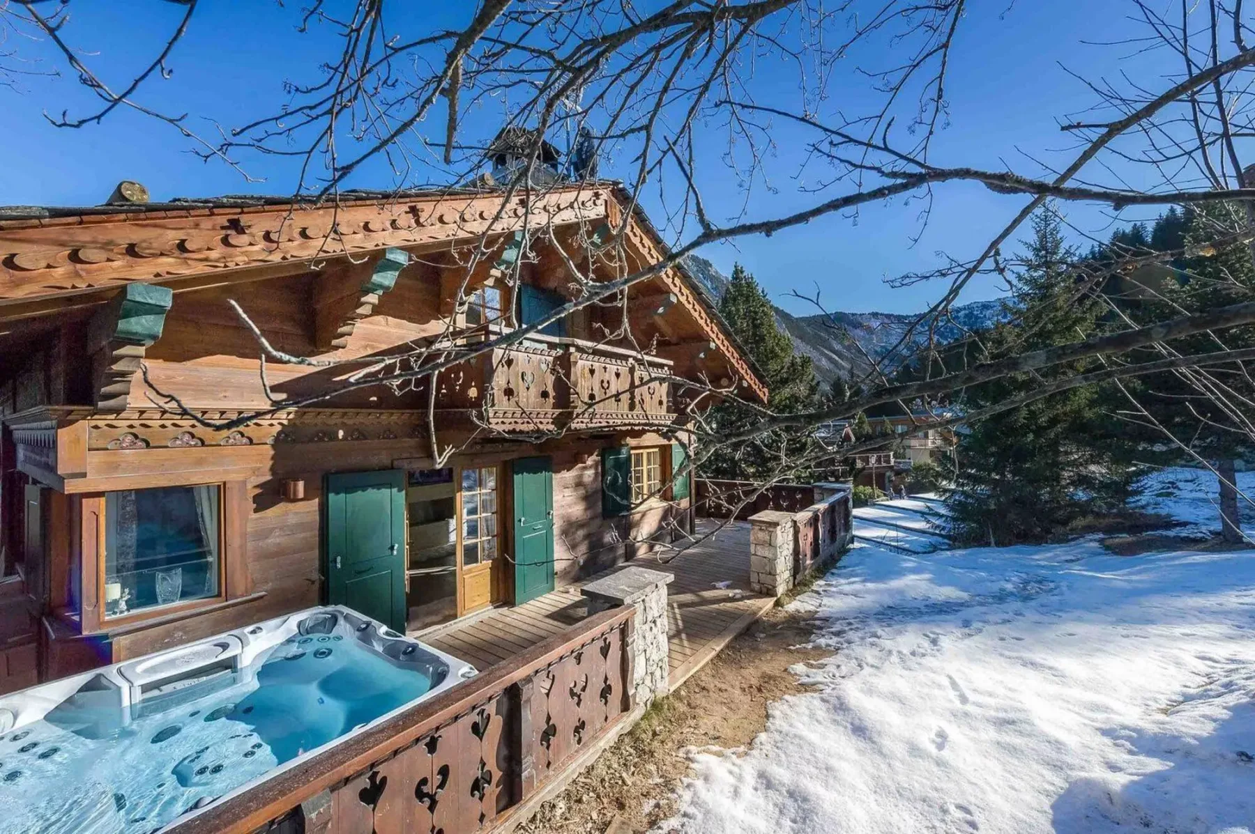 Un chalet de madera con una bañera de hidromasaje al aire libre junto a un patio nevado.