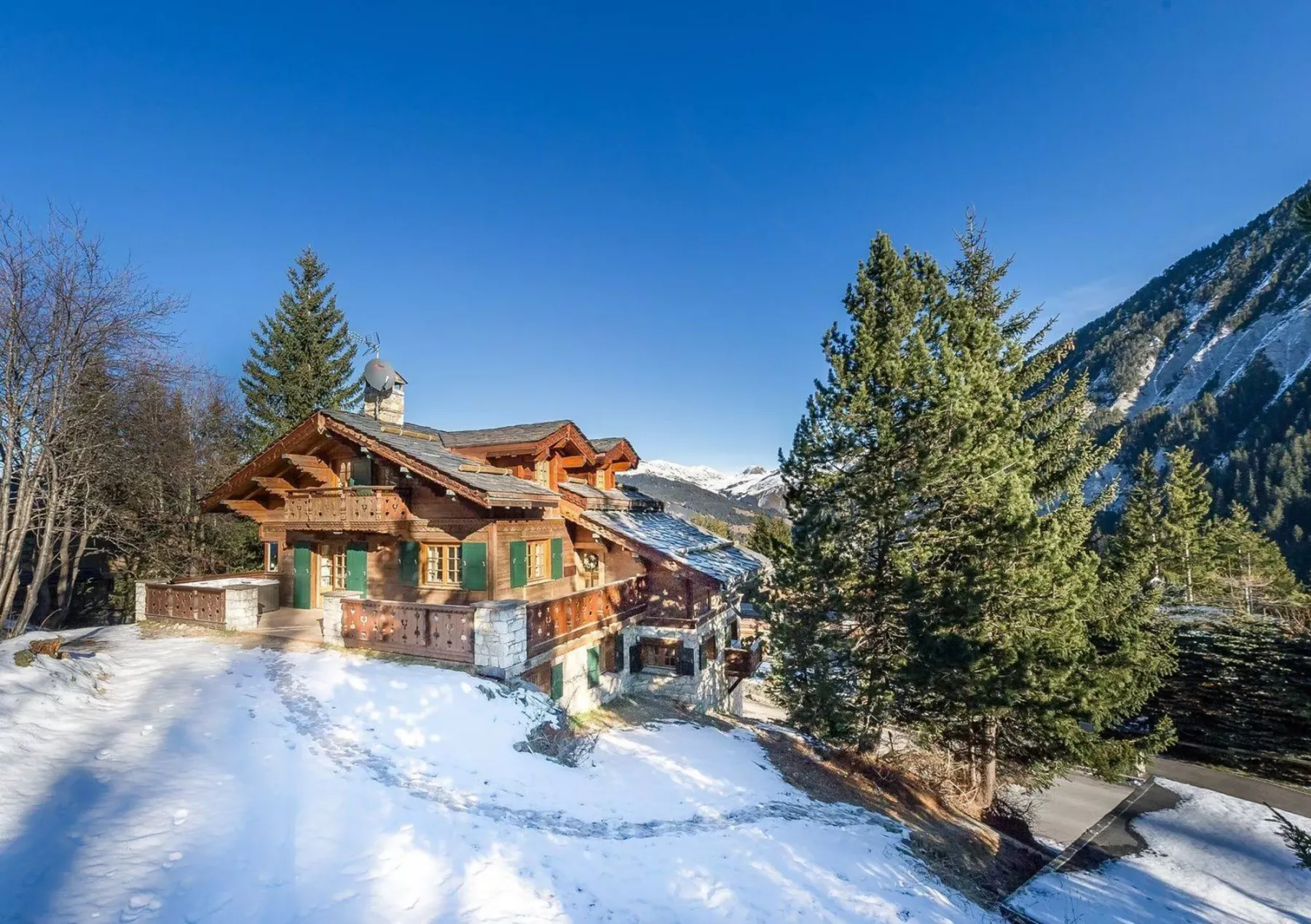 Un chalet de madera se encuentra entre árboles cubiertos de nieve bajo un cielo despejado de montaña.