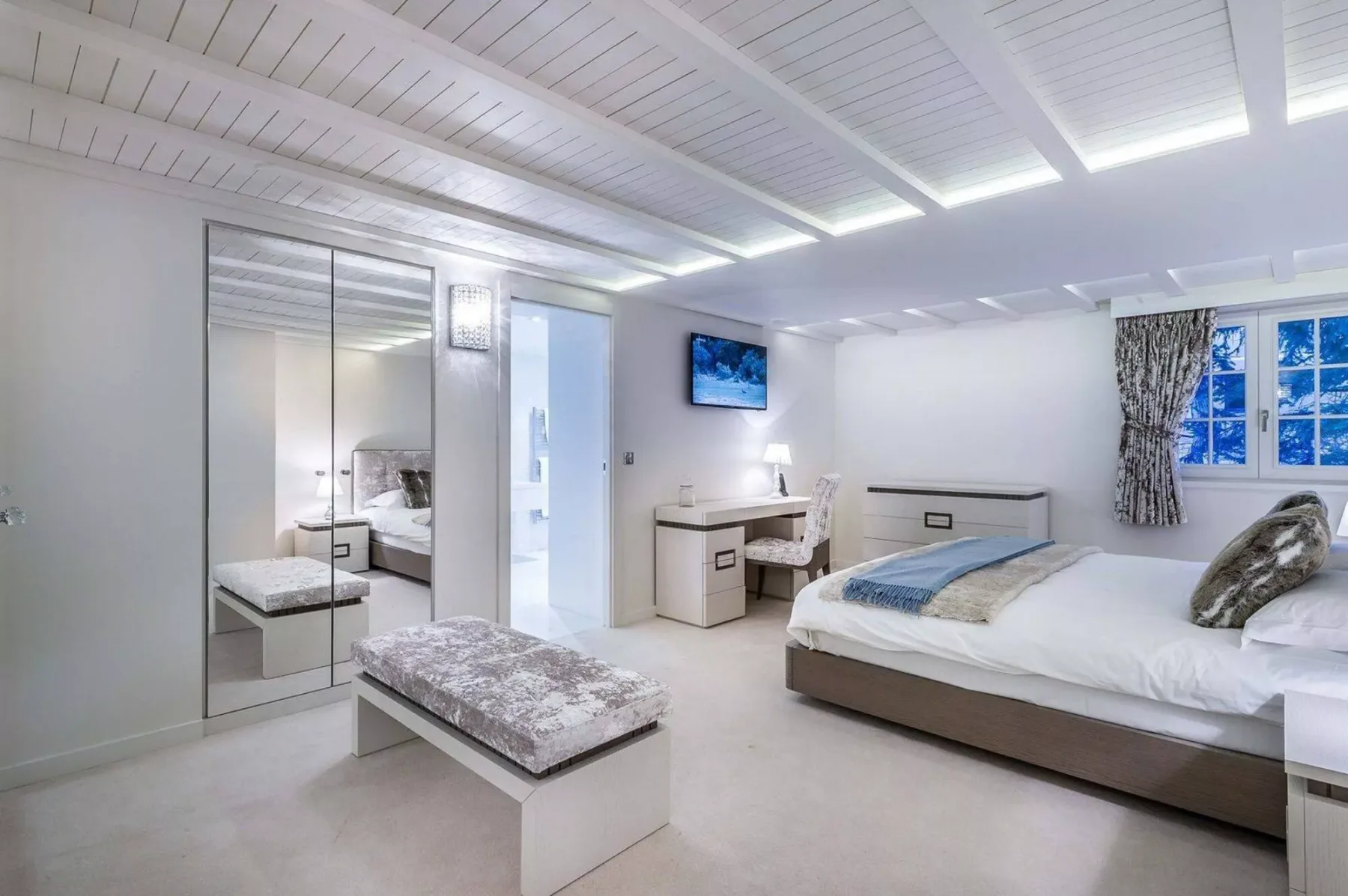 Un dormitorio luminoso con una cama grande, armarios con puertas de espejo y un escritorio.