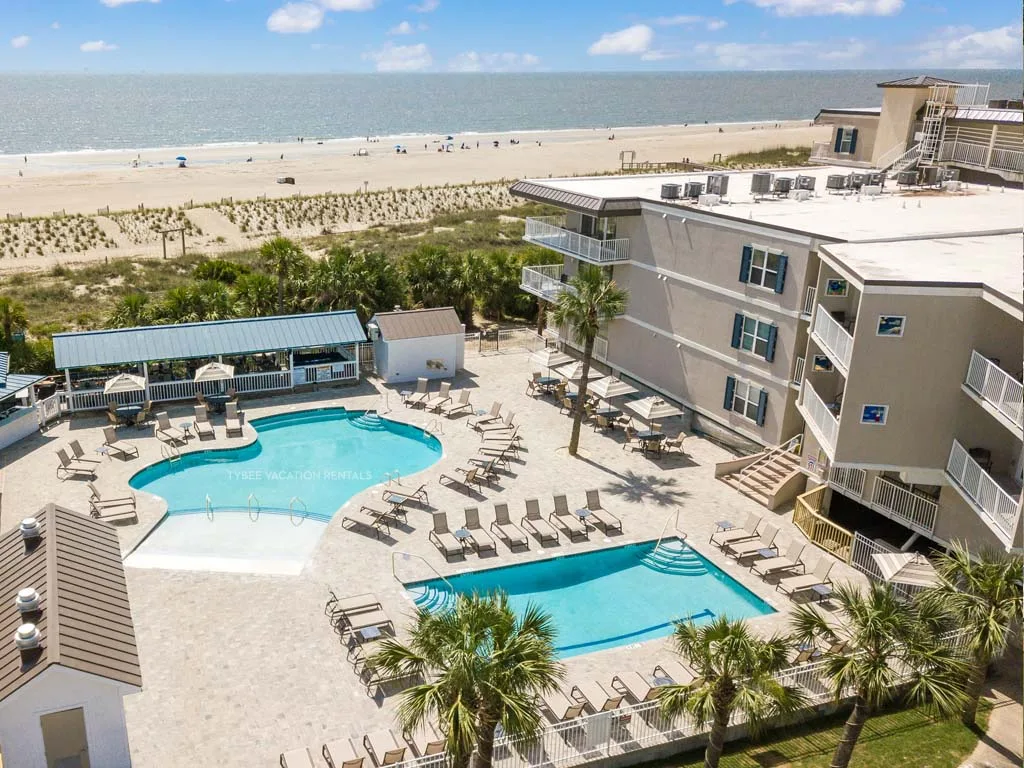 Aerial view of a beachfront resort with two swimming pools and the ocean beyond.