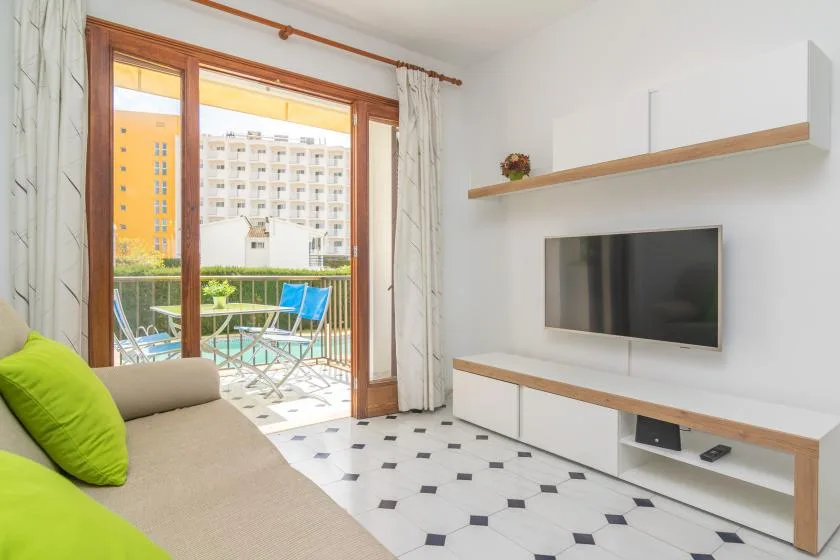 A bright living room opens onto a balcony, with a television mounted on the wall.
