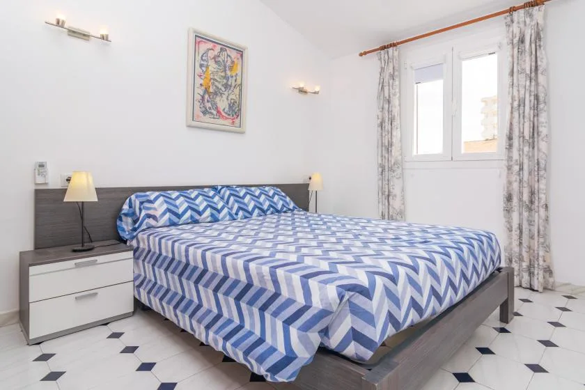 A bedroom with a bed covered in blue and white patterned bedding beside a window.