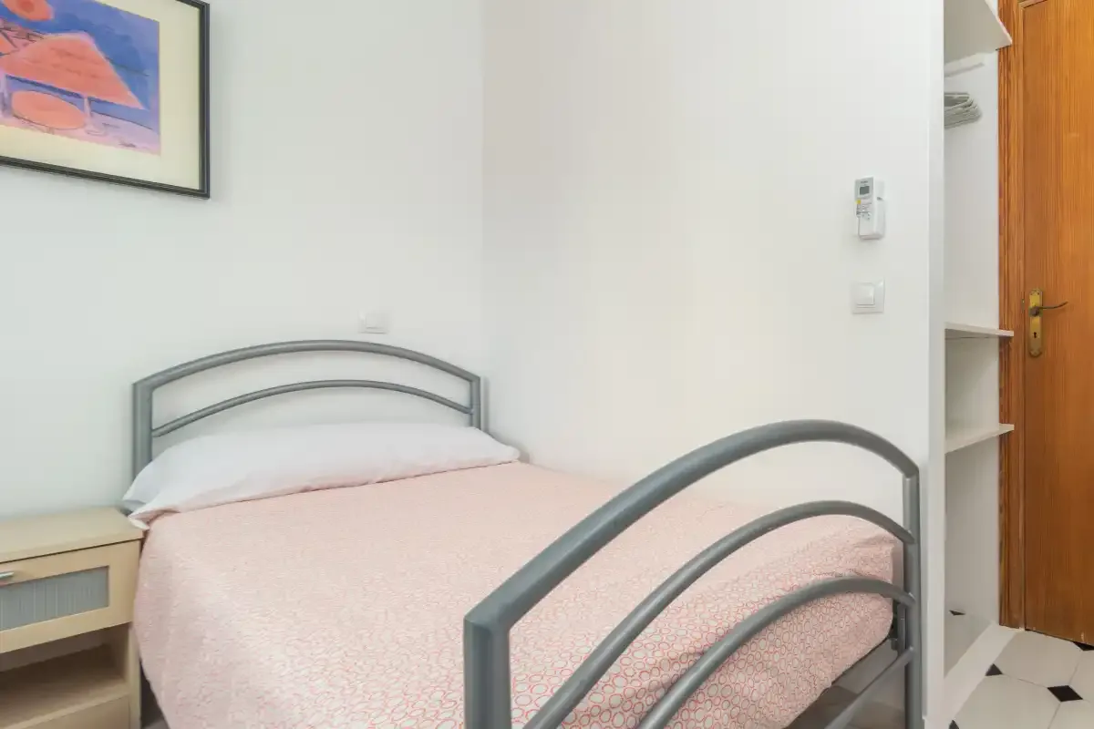 A bedroom with a bed, pale pink bedding, and a framed picture on the wall.