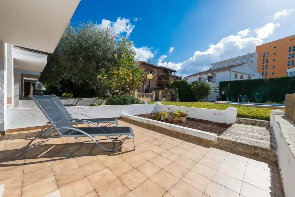 A tiled outdoor patio has a reclining lounge chair beside a planted garden.