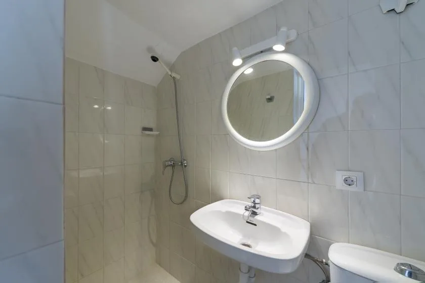 A tiled bathroom with a sink, illuminated mirror, and shower.