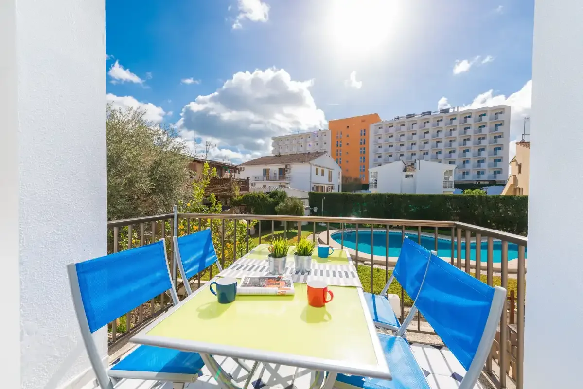 A balcony dining area overlooks a swimming pool and nearby buildings.