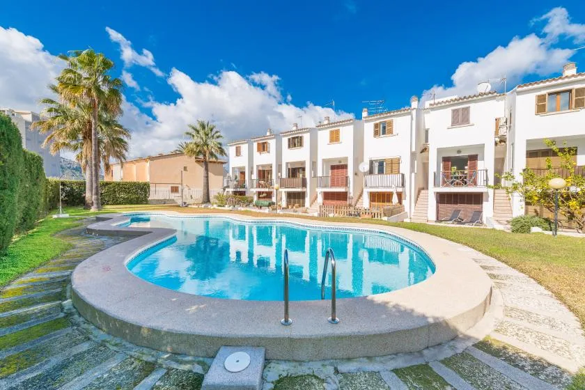 A curved outdoor swimming pool sits in front of a row of white homes.