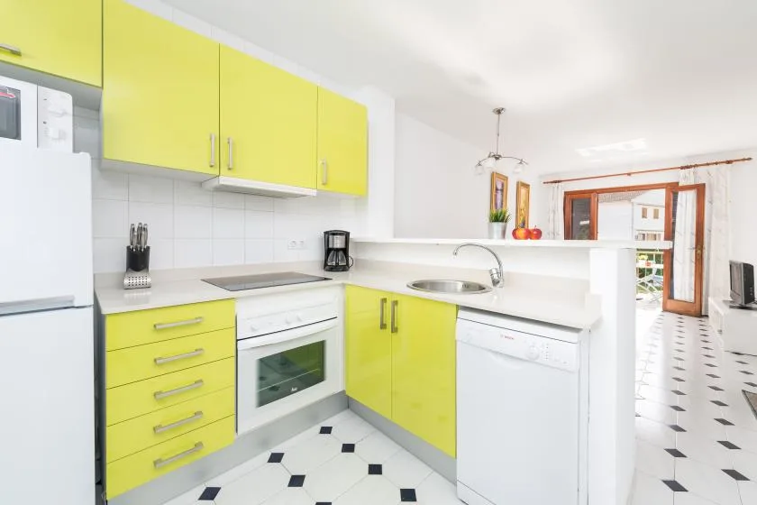 A bright kitchen with yellow cabinets, a sink, and a tiled floor.